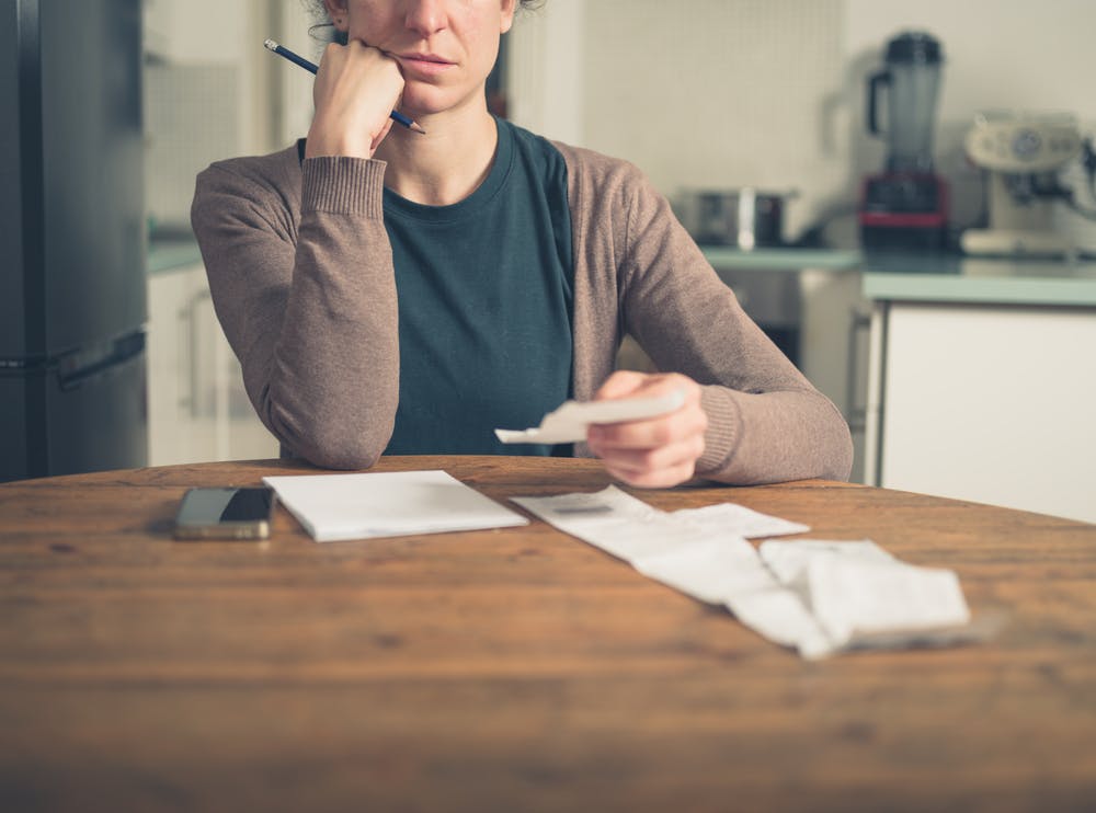 A woman is sat at a kitchen table reading her bills.